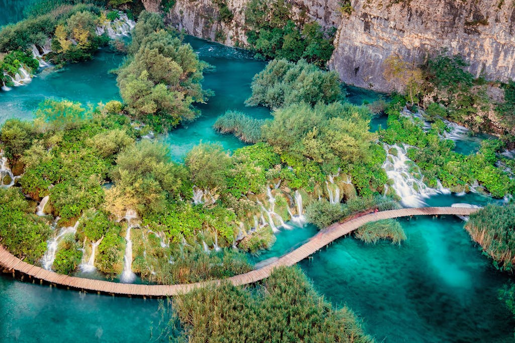A breathtaking aerial view capturing a scenic footbridge over turquoise waters and lush waterfalls.