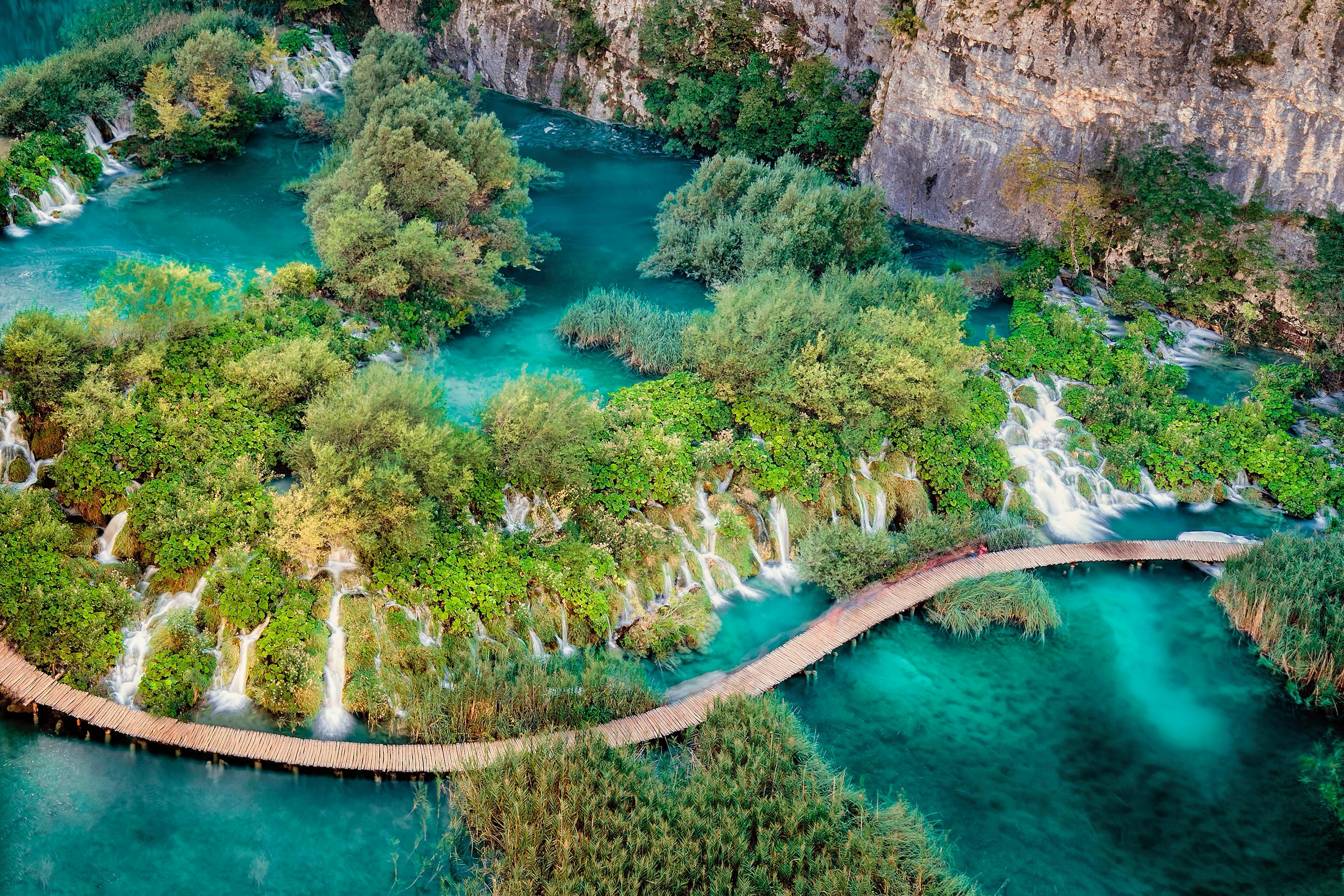 A breathtaking aerial view capturing a scenic footbridge over turquoise waters and lush waterfalls.