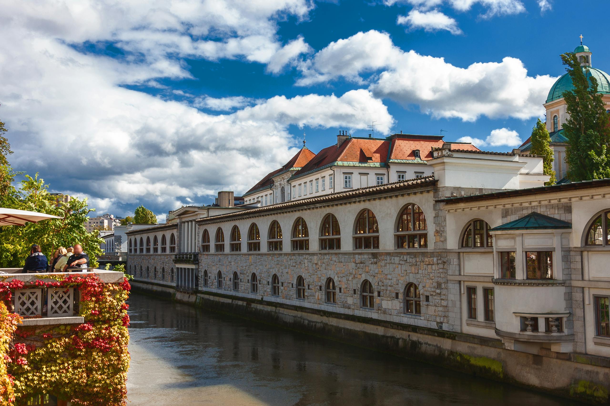 Charming riverside view of historical buildings in Ljubljana under a vibrant blue sky.