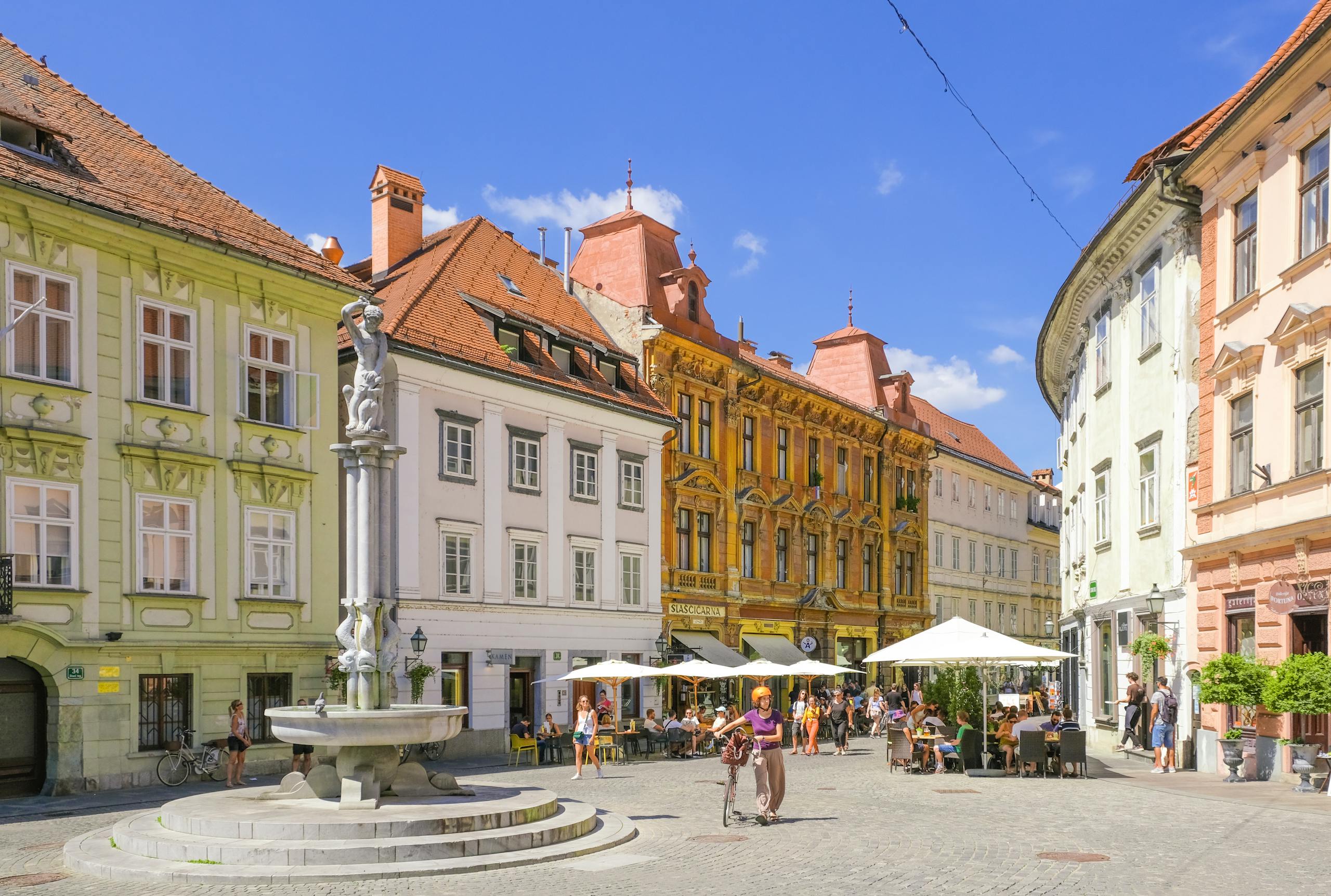 Vibrant square in Ljubljana featuring historic architecture, a fountain, and lively street cafes.